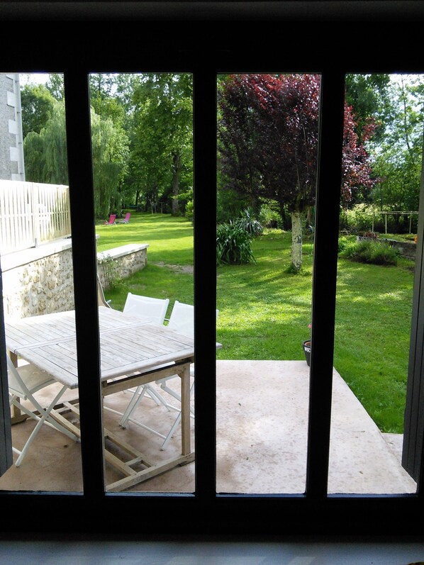 A patio with a table and chairs, a stone wall, and a view of a well-maintained garden with grass, trees, and a wooden fence. - At the water wire Perigord (Lisle)