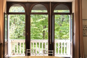 Une chambre dotée d’un balcon, de grandes fenêtres en arc de cercle et offrant une vue sur la verdure environnante.