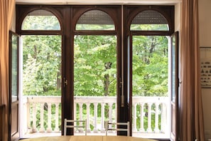 A room with a balcony, large arched windows, and a view of greenery outside.