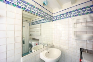 A bathroom with a large mirror, a sink, and a washing machine in the background.