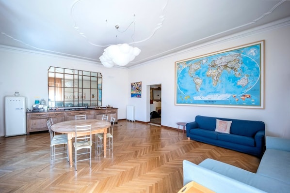 A spacious living area with a wooden herringbone floor, a dining table with chairs, a blue sofa, and a large world map on the wall.