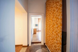 A hallway with a patterned wall, a wooden floor, and a door leading to another room.
