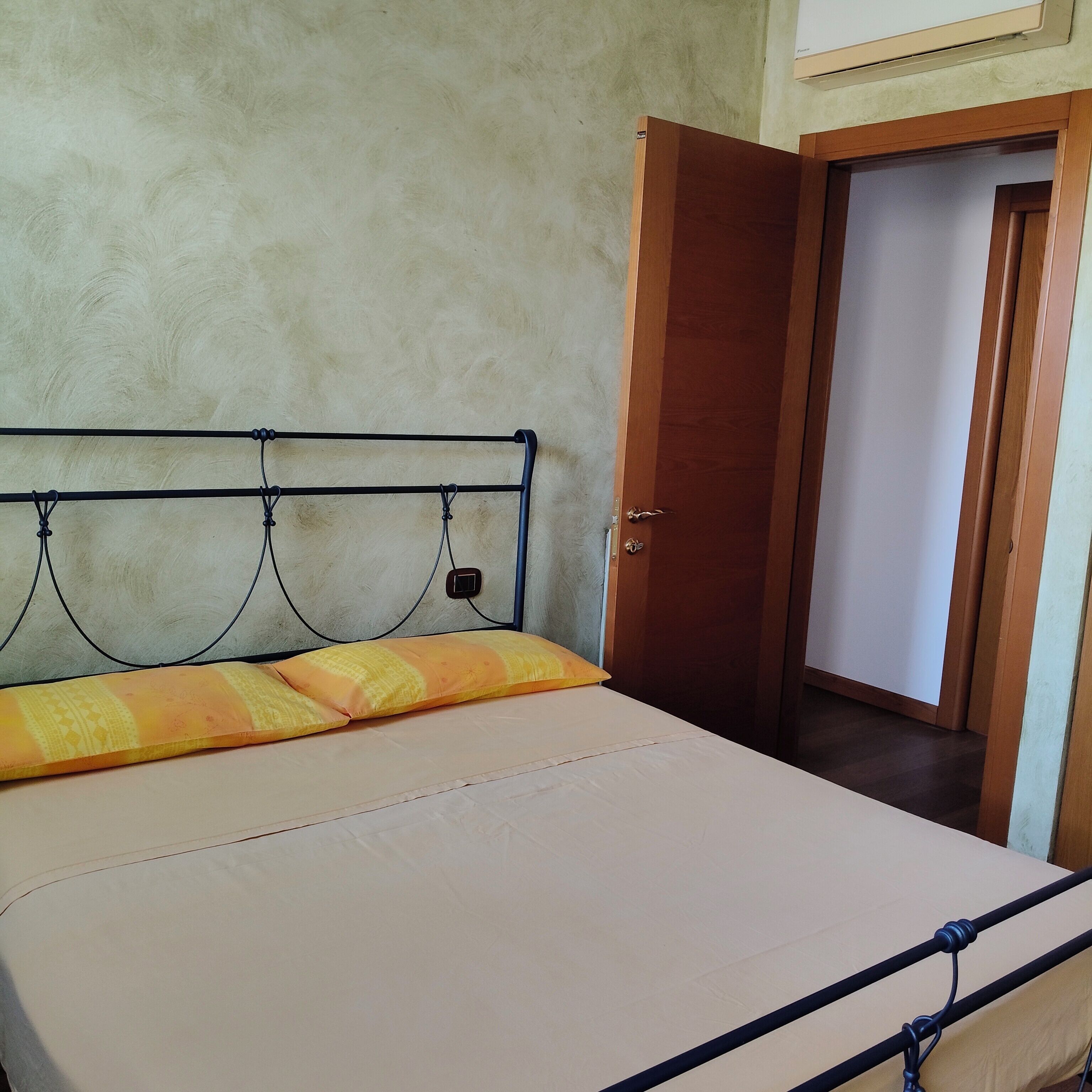 A bed with a metal frame, a plain wall, and a wooden door.