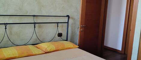 A bed with a metal frame, a plain wall, and a wooden door.