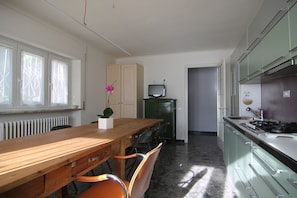 A kitchen with a wooden table, chairs, a green cabinet, a stove, and a TV.