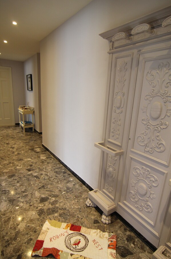 A hallway with a marble floor, a white door, a small table with a chair, and a decorative cabinet with intricate designs.
