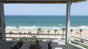 A wooden table with chairs on a balcony overlooking a beach with palm trees and a clear view of the ocean. - ALICANTE, GREAT VIEWS, SUN FOUR SEASSON AND BEACH (3 BEDROOMS) WIFI (Urbanova)