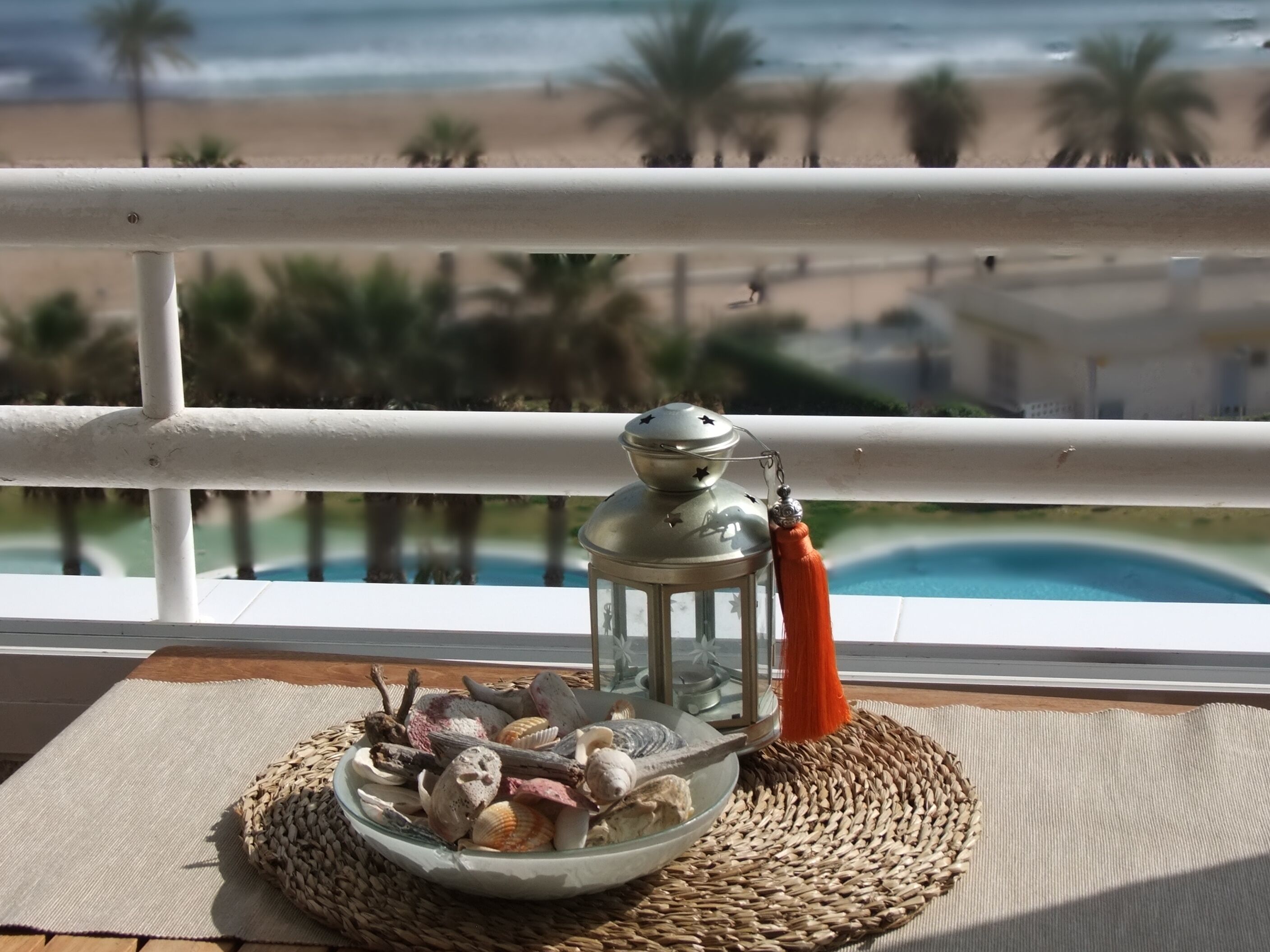A balcony with a view of the beach and ocean, a decorative lantern, and a bowl of seashells.