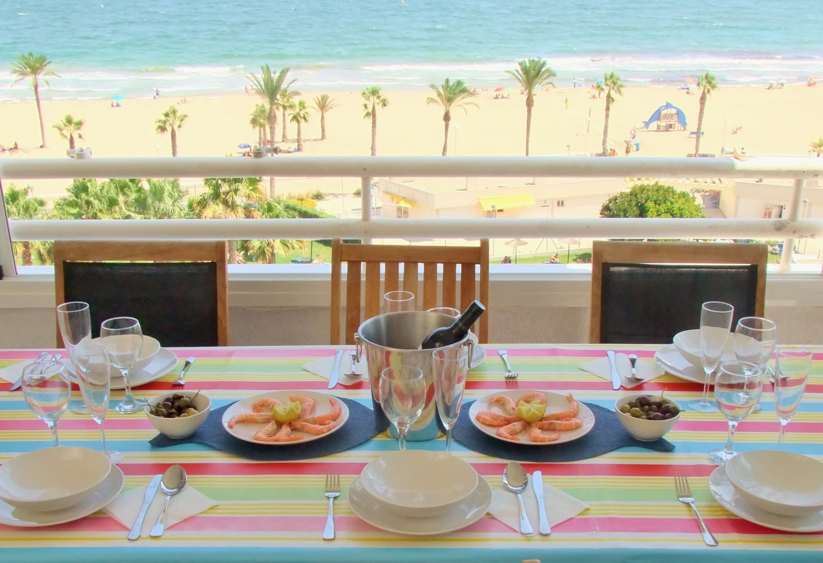 Mesa para dos personas con vista a la playa y palmeras.