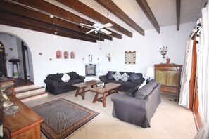 A living room with two sofas, a coffee table, and a fireplace. There is a ceiling fan and a chandelier.