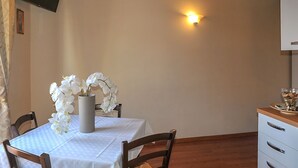 A dining area with a table set for two, a vase of white orchids, a wall-mounted TV, and a wall sconce. - Bellini Apartment with Balcony   (Catania)