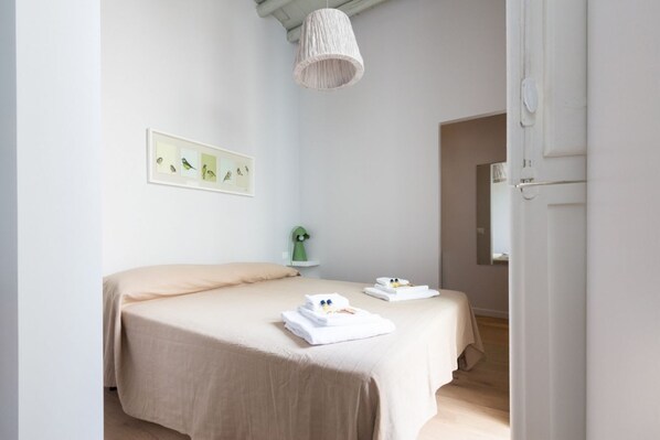 Een slaapkamer met twee bedden, een hanglamp, een ingelijst schilderij aan de muur en een deur naar een andere kamer.