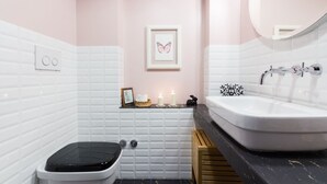 Een badkamer met witte betegelde wanden, een zwart toilet, een wit wastafelmeubel en een spiegel.