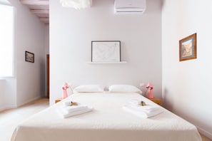 Une chambre d’hôtel avec un grand lit, du linge de lit blanc, une œuvre d’art encadrée au mur et une petite table de chevet avec une lampe.