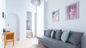 Een moderne woonkamer met een grijze bank, een houten bijzettafeltje en twee posters aan de muur.