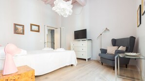 Een slaapkamer met een bed, een dressoir, een stoel, een televisie en een lamp.