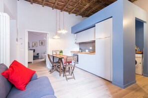 A modern kitchen with a blue accent wall, wooden flooring, and a dining area with a table and chairs. - Ideal Apartment Navona Square (Roma)