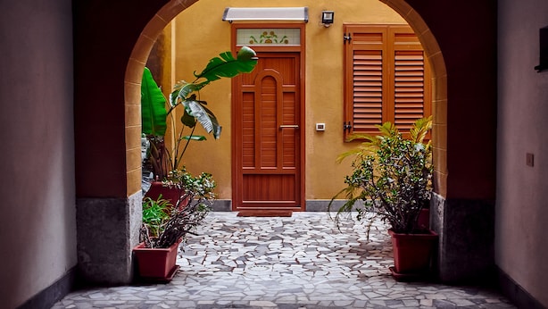 Um pátio com piso de azulejos, porta de madeira e plantas em vasos.