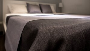 Cama bem arrumada com colcha cinza e almofadas, cabeceira branca e um quadro na parede.