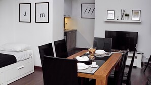 Uma sala de jantar moderna e bem iluminada, com uma mesa de madeira posta para dois, cozinha ao fundo e quadros nas paredes.