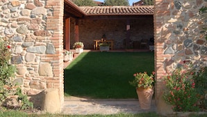 A stone archway leading to a covered patio with a tiled roof, surrounded by a well-maintained lawn and potted plants. - Stone corner in Barcelona (Corró d'Avall)