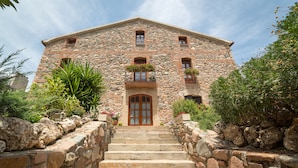 A stone building with a central entrance, multiple windows, and a staircase leading to the entrance. - Stone corner in Barcelona (Corró d'Avall)