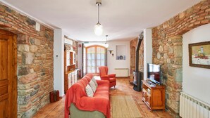 A cozy living room with a stone wall, a red sofa, a television, and a fireplace. - Stone corner in Barcelona (Corró d'Avall)