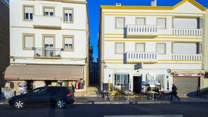 A street view with a row of buildings, including a shop with a visible storefront and outdoor seating area. - Fertile Dreams-Freedom 10 meters from the beach (Nazaré)