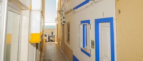 Une ruelle étroite pavée, bordée de bâtiments aux façades bleues et blanches, avec une porte bien visible et un lampadaire.