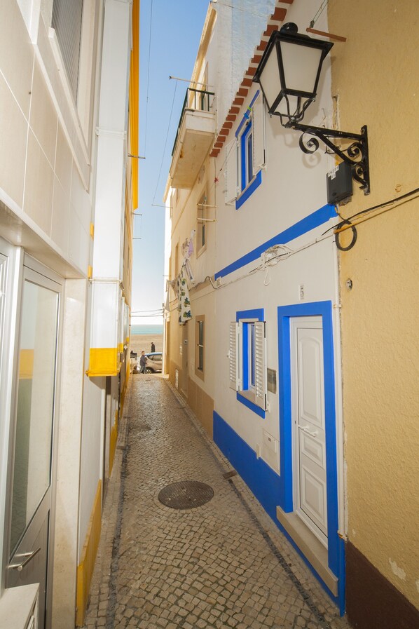 A narrow cobblestone street flanked by buildings with blue and white facades, a visible door, and a street lamp.