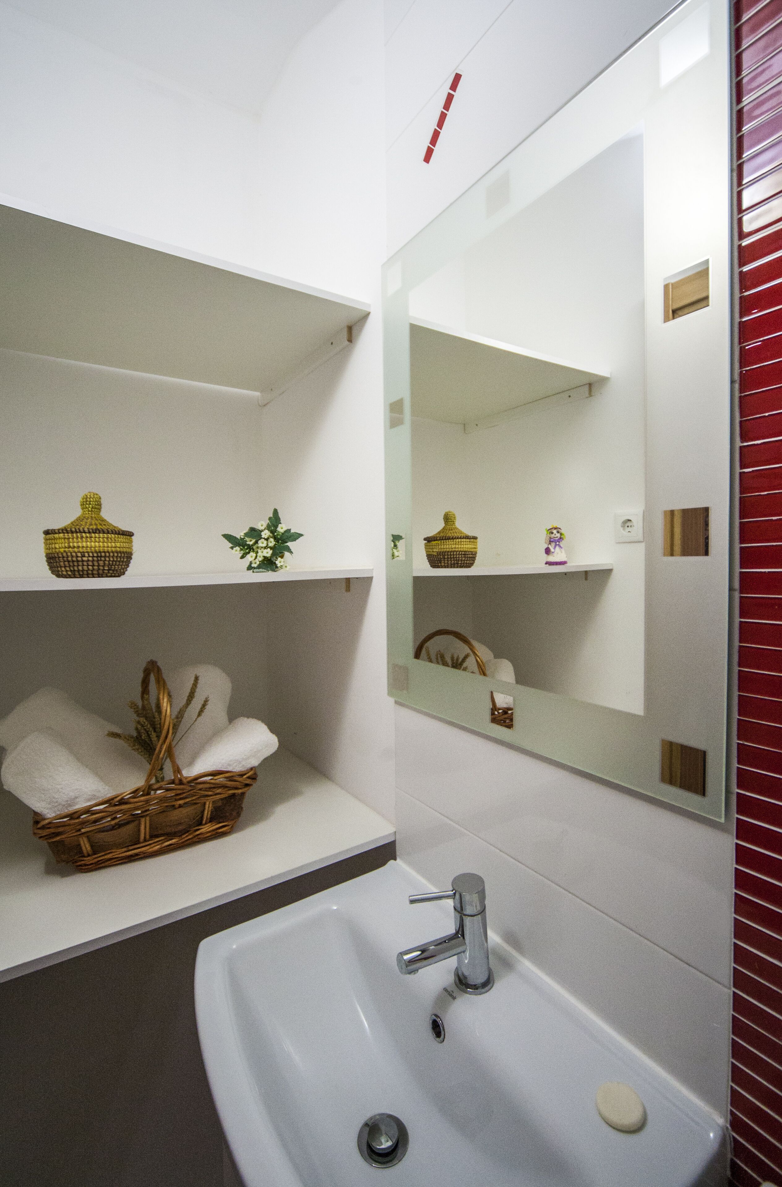 Ein Badezimmer mit einem weißen Waschbecken, einem Spiegel und Regalen mit Körben und einer Pflanze.