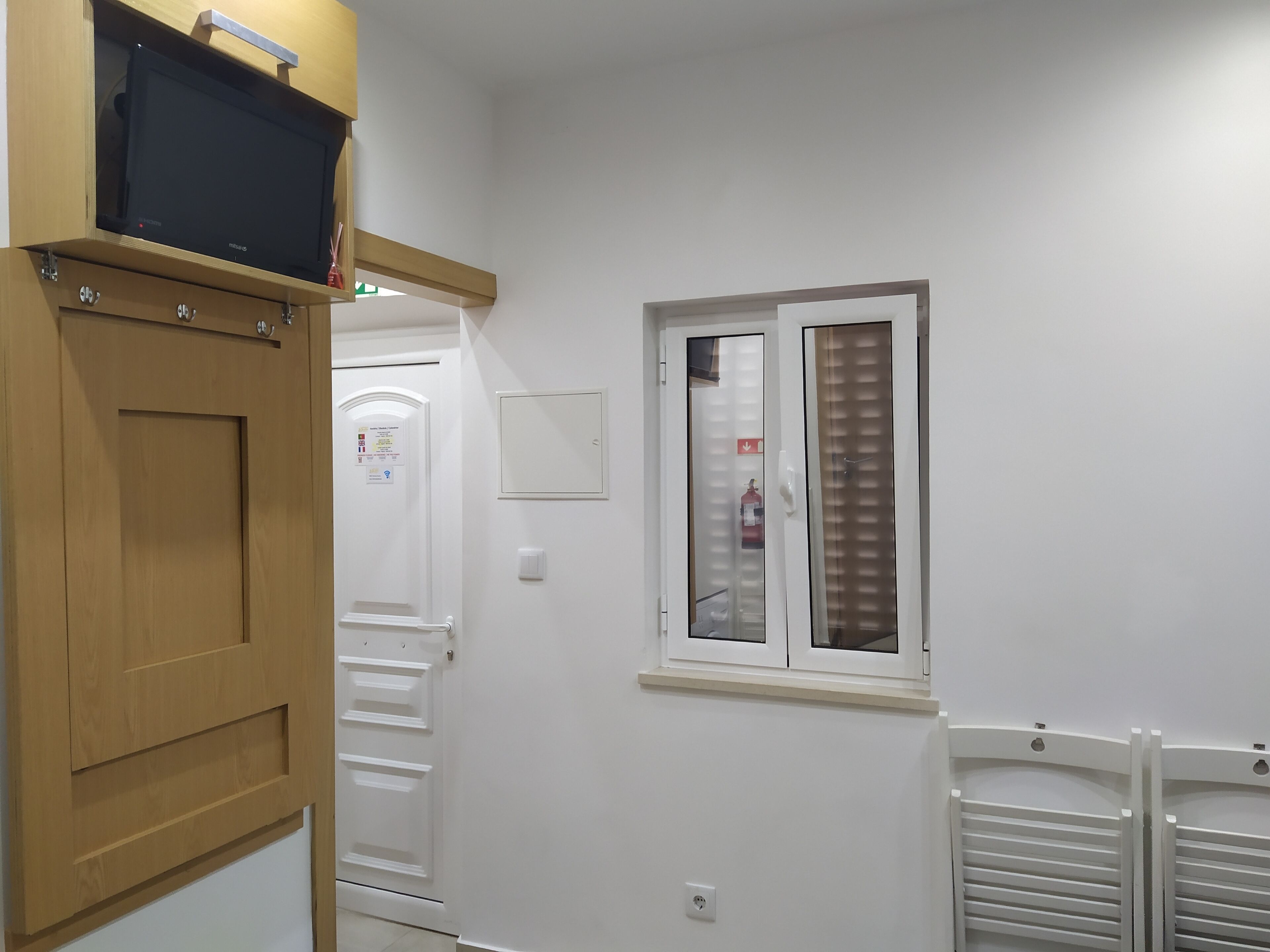 A hallway with a wooden door, a window with blinds, a white wall, and a white radiator.