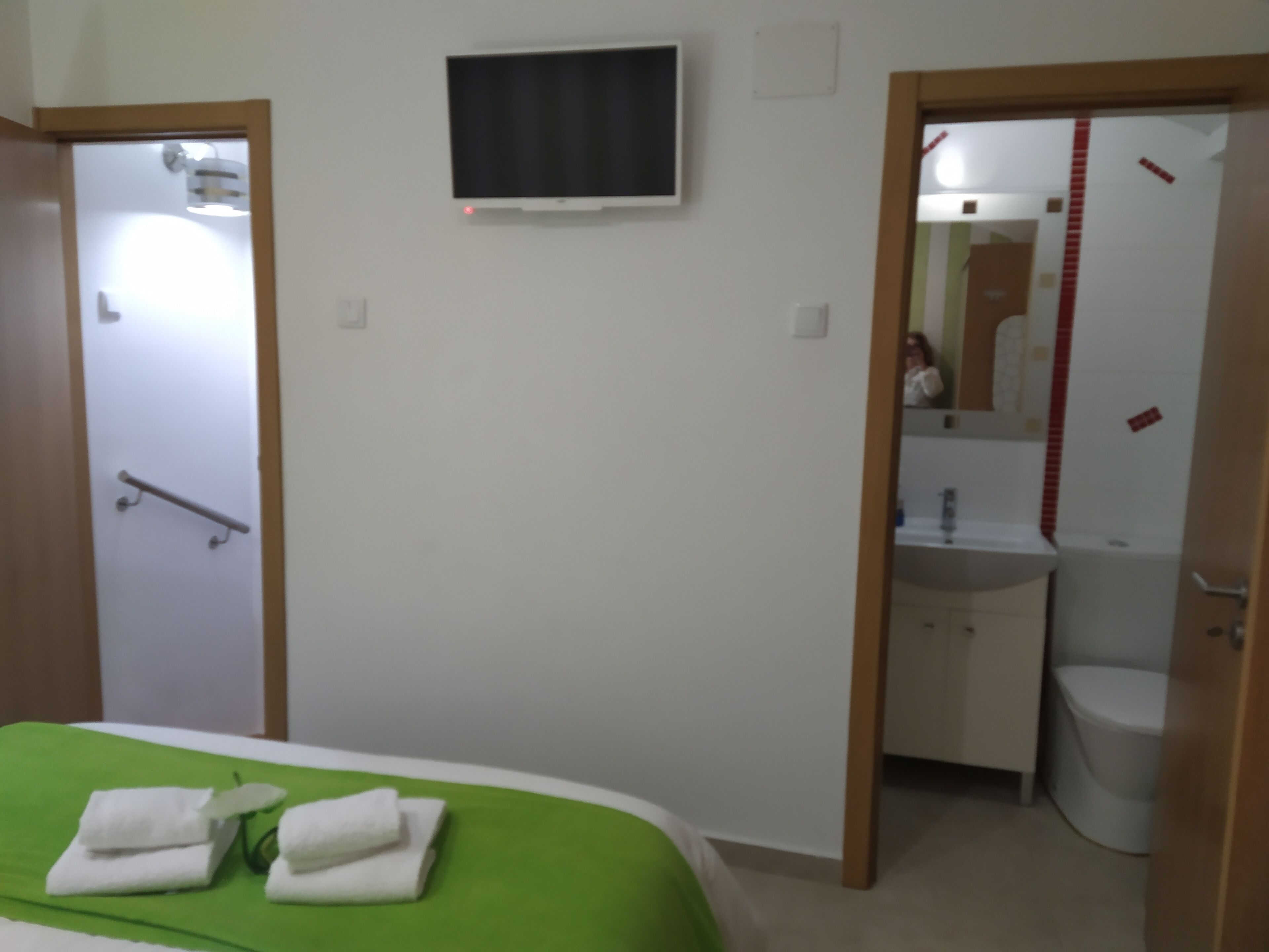 A hotel room with a bed, a television mounted on the wall, a bathroom with a sink and toilet, and a shower area.