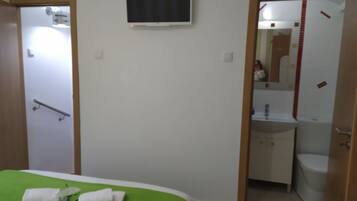A hotel room with a bed, a television mounted on the wall, a bathroom with a sink and toilet, and a shower area.