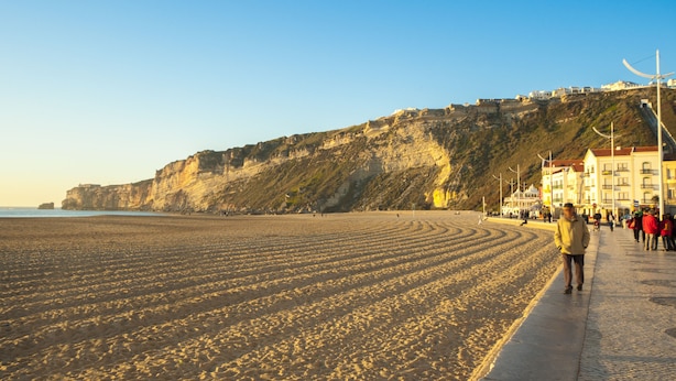 A coastal beach with a promenade, buildings, and cliffs. - Fertile Dreams-Freedom 10 meters from the beach (Nazaré)