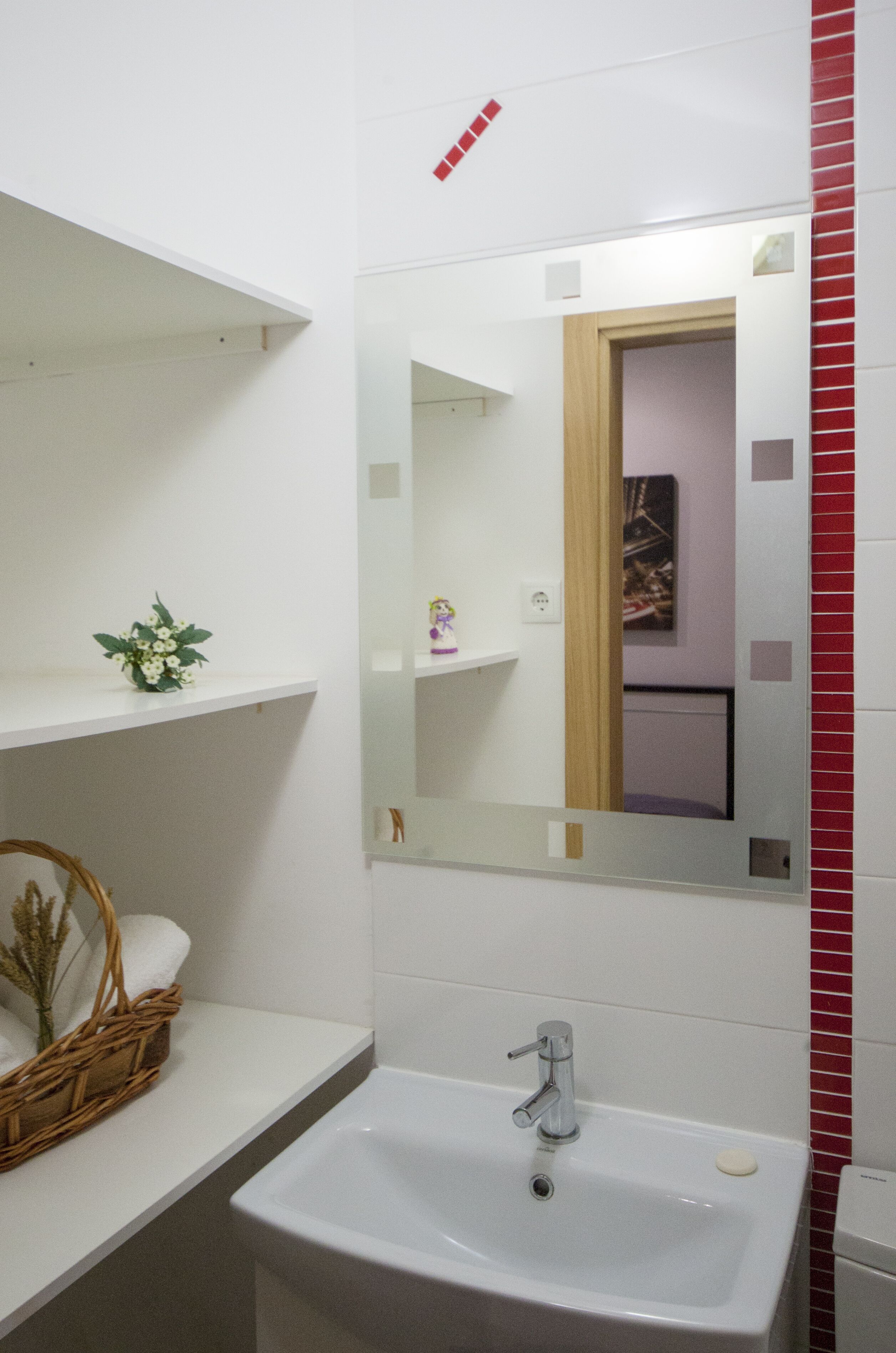 Une salle de bain avec un lavabo blanc, un miroir et des étagères contenant des articles de toilette.