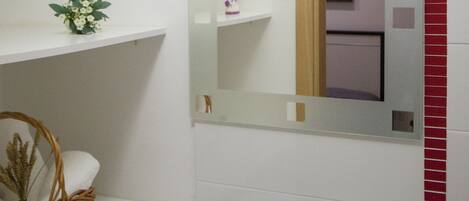 Un baño con lavamanos blanco, un espejo y repisas con artículos de aseo.