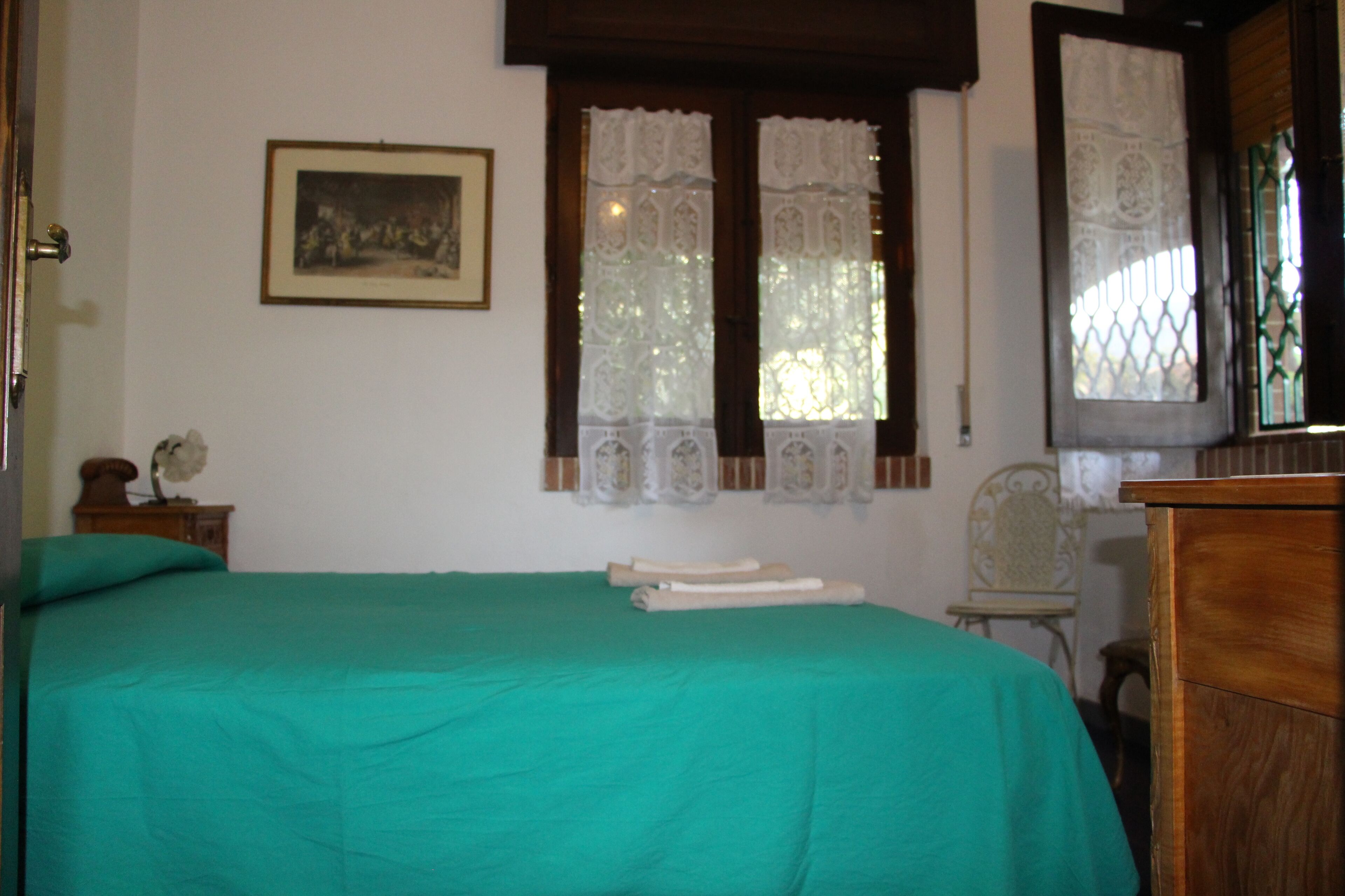 Ein Zimmer mit einem Bett, einem hölzernen Schminktisch, einem Stuhl und einem Fenster mit Spitzenvorhängen.