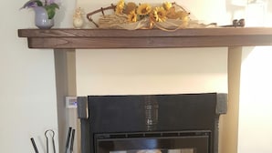 Une cheminée avec un foyer en pierre, une étagère décorative au-dessus du manteau et un thermostat fixé au mur.