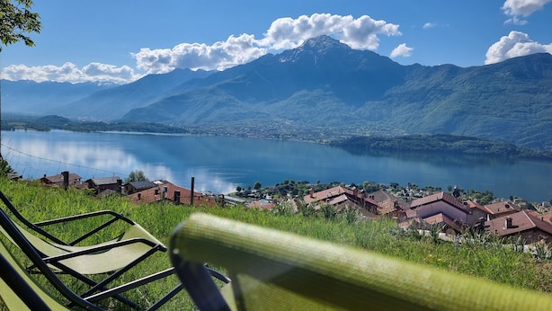 Une vue sur un lac, avec des montagnes en arrière-plan, une chaise au premier plan et un petit village avec des maisons.
