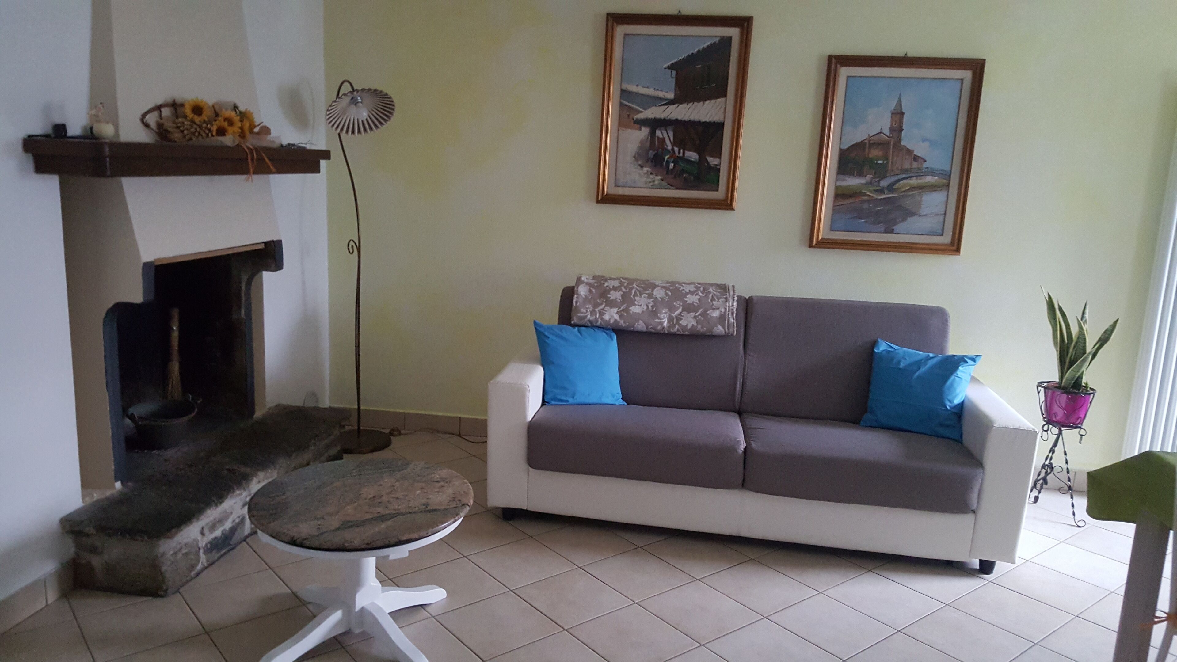 En stue med en sofa, et lille bord, en pejs og to billeder i rammer på væggen.