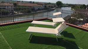 Un balcone con erba sintetica e due poltrone relax, vista su un fiume e edifici residenziali.