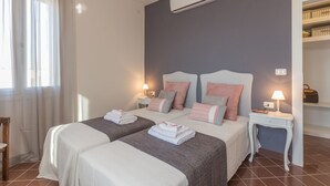 Camera d'albergo con due letti, un comodino con lampada, un armadio e un condizionatore.