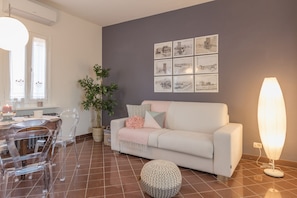 Un salon moderne avec un canapé blanc, des chaises transparentes, une table à manger, une plante en pot et des œuvres d’art murales.