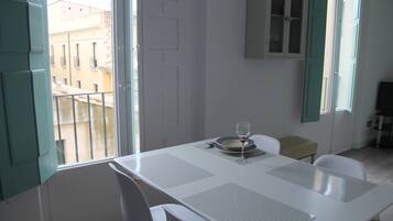 Un comedor con una mesa dispuesta para dos, una ventana con vistas a edificios y un aparador con puertas de cristal.
