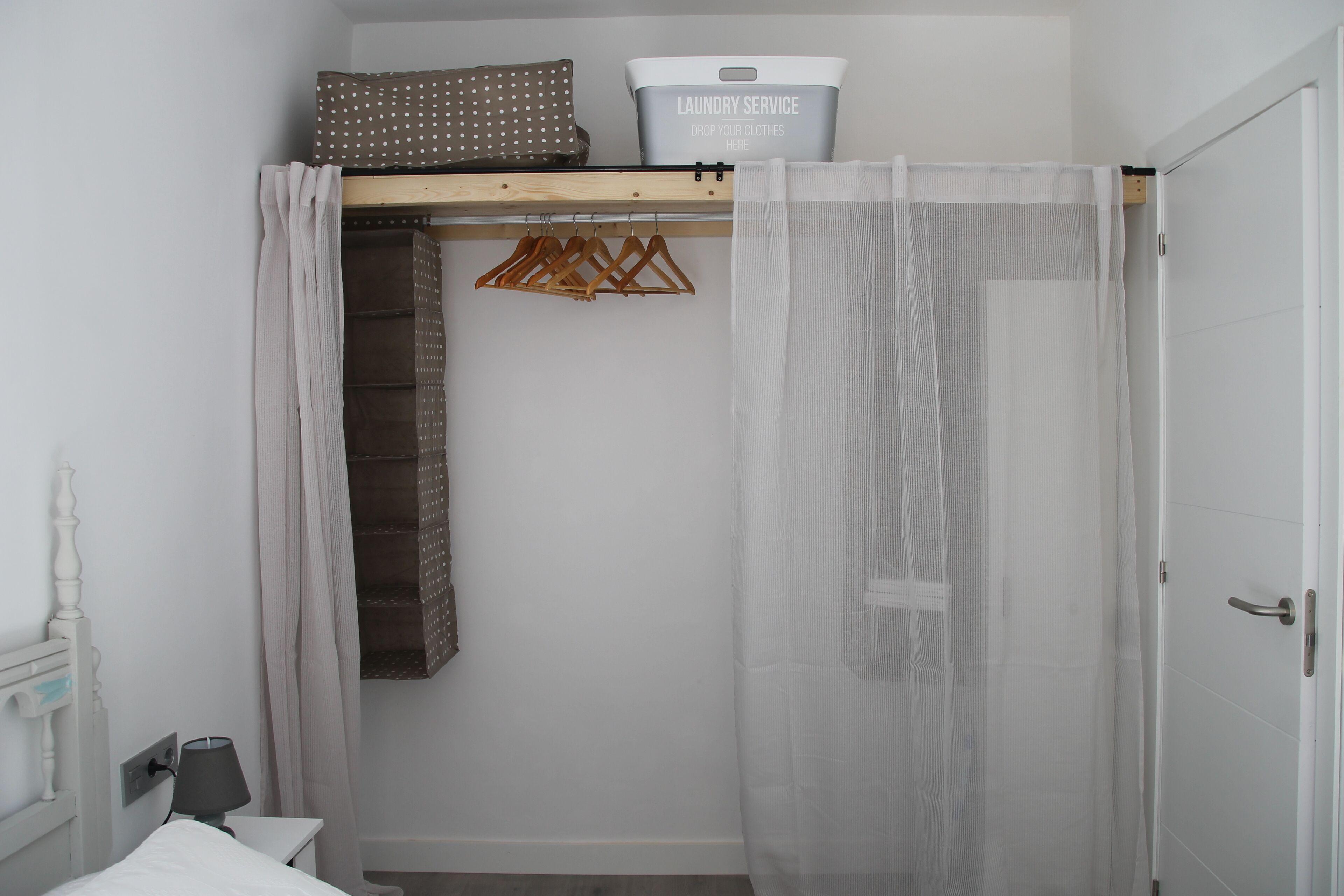 Une chambre à coucher comprenant un lit, une armoire, un portant à vêtements et un panier à linge.
