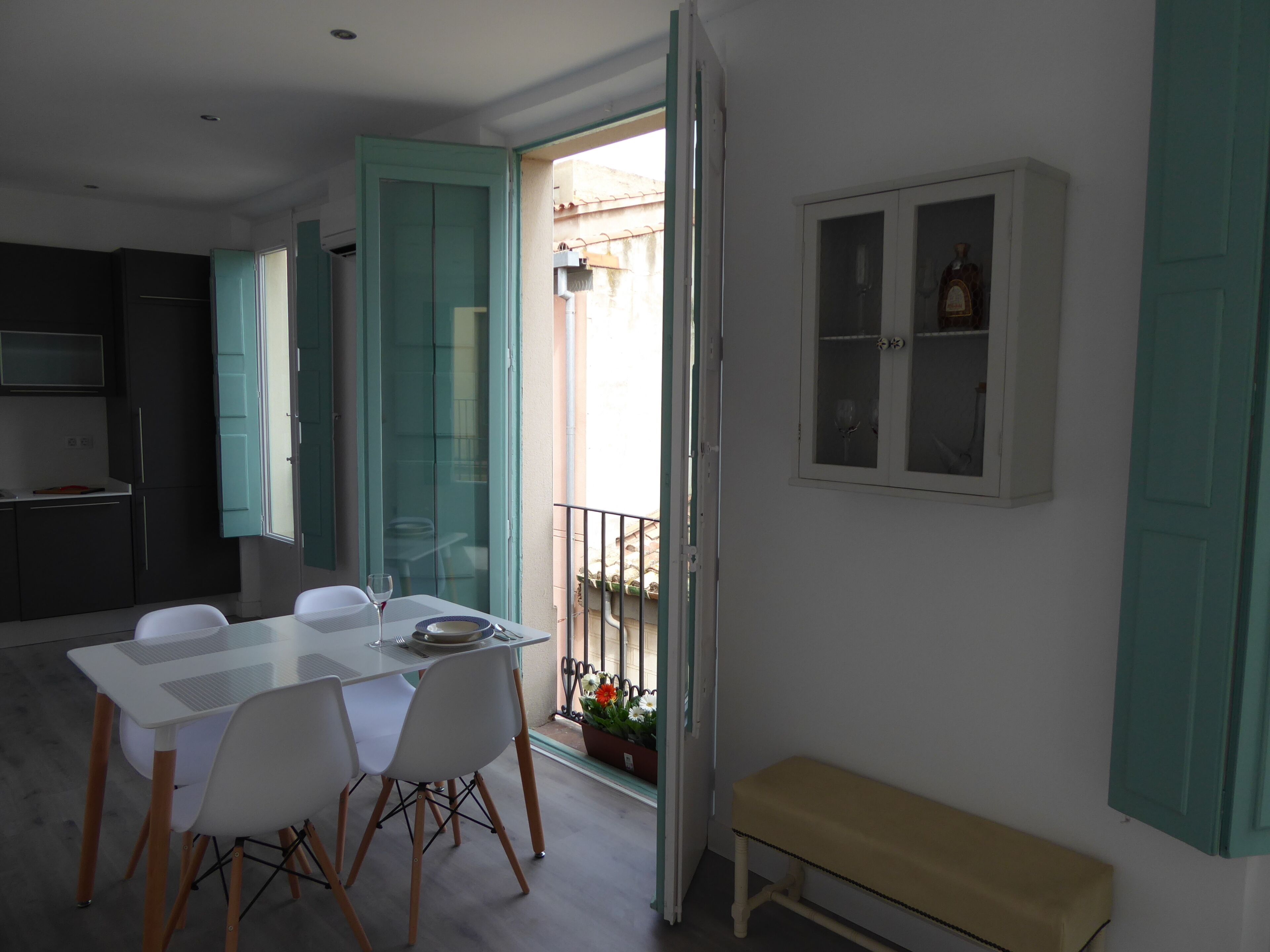 Una cocina moderna con armarios blancos, una mesa de comedor con sillas y un pequeño balcón con plantas en macetas.