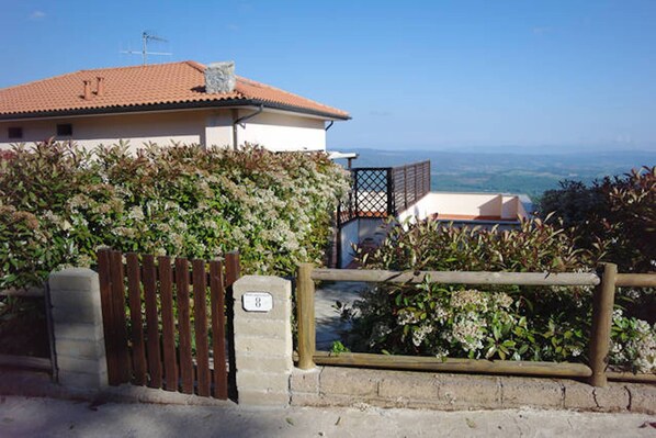 A building with a tiled roof, a wooden gate, and a view of the landscape. - Watching The Horizon in residence with swimming pool for a fee (Monteverdi Marittimo)