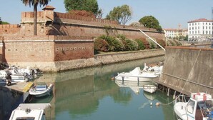 A historic fort with a moat, boats docked in the water, and a building with a red roof in the background. - Watching The Horizon in residence with swimming pool for a fee (Monteverdi Marittimo)