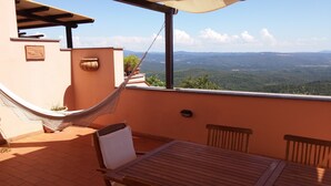A balcony with a hammock, wooden table, and chairs, overlooking a mountainous landscape. - Watching The Horizon in residence with swimming pool for a fee (Monteverdi Marittimo)